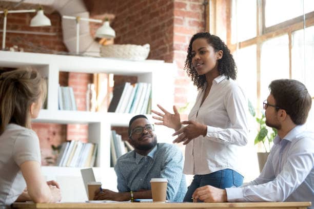 Ambitious smart african black female employee speaking at diverse meeting share creative idea opinion at group briefing while jealous envious skeptical male coworkers looking listening to colleague